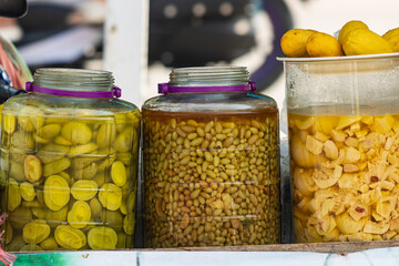 Three jars of food sit on a table, including pickles, beans, and fruit