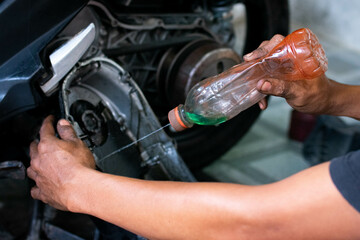 Close up of a mechanic’s hands cleaning a scooter’s CVT housing using a special cleaning liquid during routine maintenance.