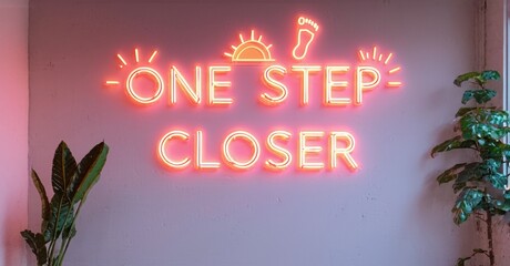 Neon sign displays motivational phrase. Footprint, sun imagery present. Pink wall background, plants flank sides. Warm lighting.