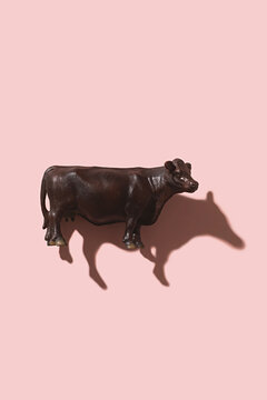 Plastic toy cow on a pink background with shadow