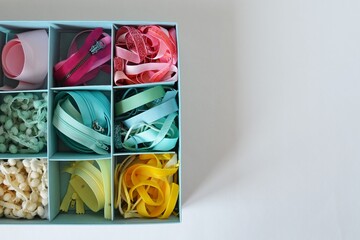 Colorful ribbons, cords and zippers in blue box on white background