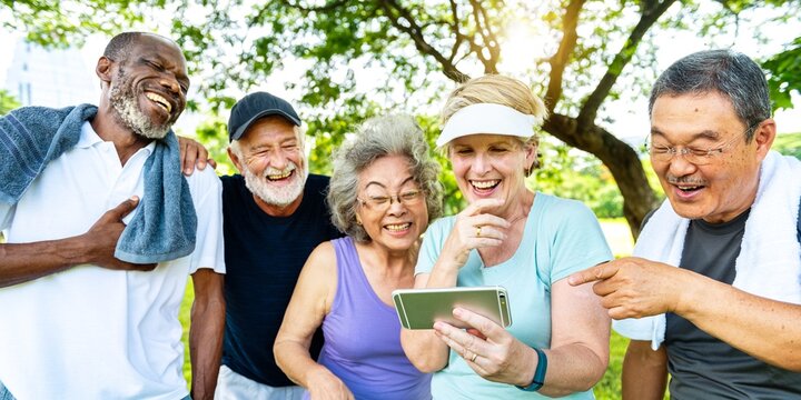 Group of diverse elderly friends enjoying time outdoors, watch exercise video. Elderly friends enjoy exercise video in outdoor park. Happy diverse elderly friends in park, watch video after exercise