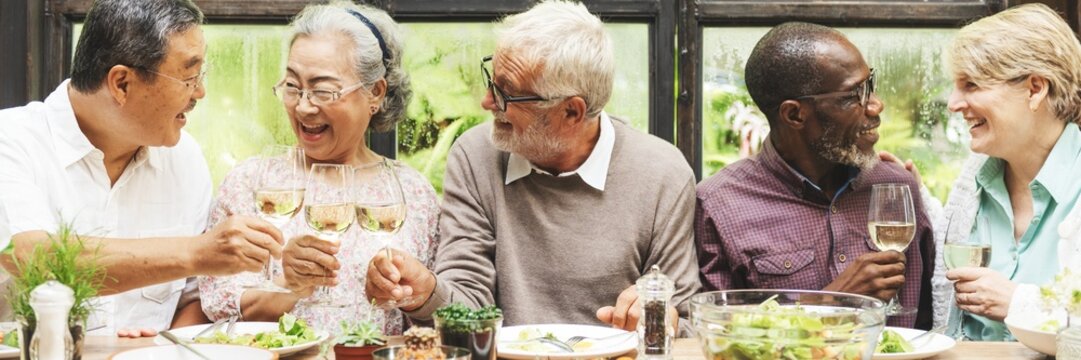 Group of diverse seniors enjoying a meal together, sharing laughter and wine. Elderly friends, diverse gathering, joyful meal, happy seniors, wine glasses. Senior friends drinking with wine for lunch. - Powered by Adobe