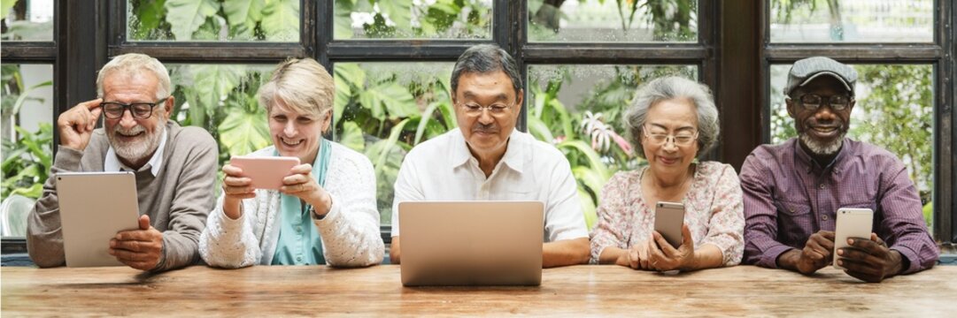 Diverse group of seniors using technology. Elderly men and women with devices. Seniors with tablets and laptops. Multicultural elderly tech users. Senior people using digital devices and social media. - Powered by Adobe