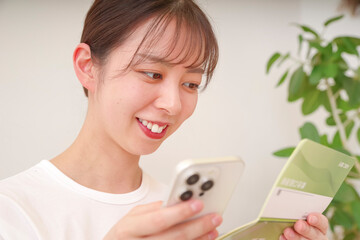 スマホと通帳を見てほほえむ女性