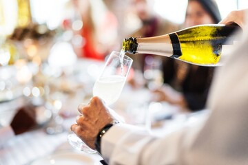 Close-up of champagne being poured into a glass. Bubbly champagne, elegant glass, and celebratory atmosphere. Champagne and glass perfect for celebrations. Man pouring champagne into glass at table