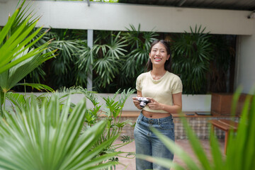 Fototapeta na wymiar Young, happy asian woman photographer smiling while holding a vintage camera in a vibrant tropical garden, surrounded by lush green plants and natural light, enjoying a serene moment in nature