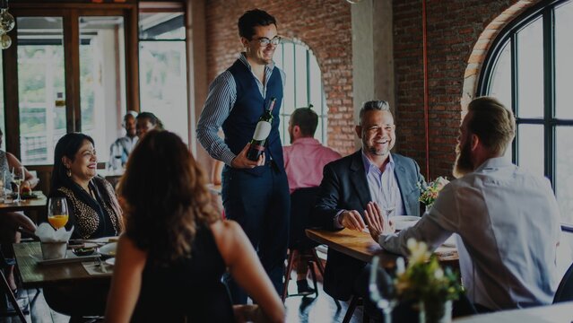 People dining in a cozy restaurant. Waiter serves wine. Diners enjoy food and conversation. Restaurant ambiance with happy diners and good service. People enjoying a meal at French bistro restaurant.