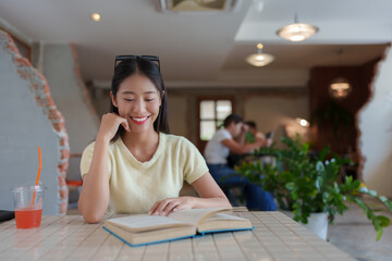 Young woman immersed in a captivating book while sipping a refreshing drink in a lively cafe,...