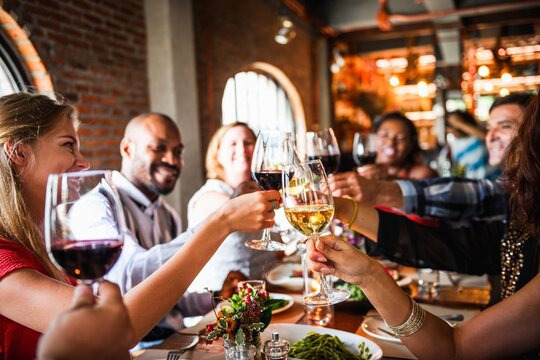 Group of people toasting with wine glasses at a lively dinner gathering. Diverse group, enjoying a meal together in a cozy restaurant setting. Happy friends toasting and celebrating at restaurant.