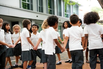 Group of diverse children holding hands in a circle outdoors. Children in school uniforms, playing and smiling. Happy students enjoying playtime together in a outdoor school. Diverse students
