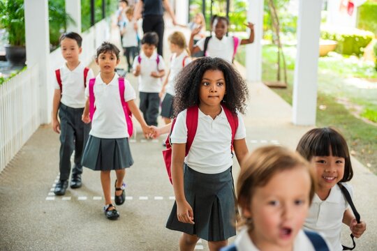 Children in school uniforms with backpacks walking in a line. Diverse group of kids, school uniforms, backpacks, walking together, school setting. First day at school for little kids.