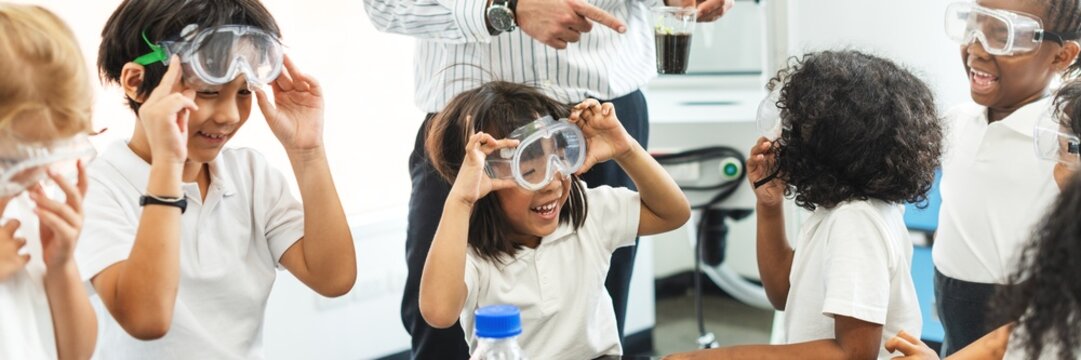 Diverse children wearing goggles in a science class, laughing and having fun. Diverse kids enjoying science experiments. Diverse elementary students engaging in a playful learning environment.