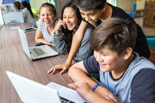 Group of kids using laptops, smiling and learning together. Diverse children engaged with technology, enjoying teamwork and education. Happy kids learning with a laptop, online education for students.