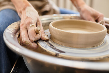 Hands expertly shape clay on the potters wheel in a bright and inviting pottery studio