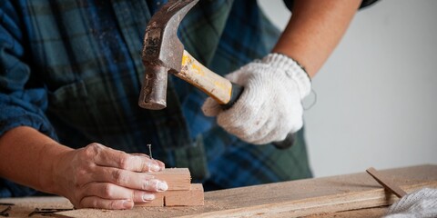 Close-up of a person hammering a nail into wood. Wearing gloves, focused on carpentry. Woodworking, hammer, and nails in action. DIY carpentry project. Woodworking and construction work concept.