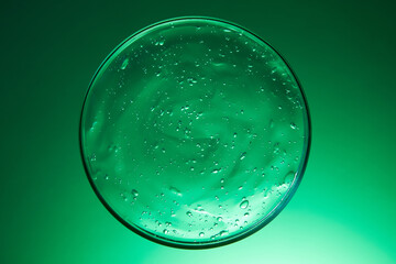 Close-up photo of cosmetic essence extracted from natural ingredients. The essence texture is transparent, with many air bubbles. The essence dish display on a green background. Laboratory concept.
