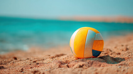 Obraz premium A vibrant yellow and white volleyball rests invitingly on the warm sandy beach, with the tranquil turquoise sea and clear blue sky providing a beautiful backdrop.