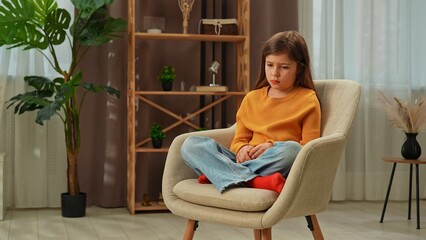 Young girl child spending evening time at home, girl sits in chair in the living room with...