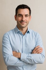 A confident man with short dark hair, wearing a crisp light blue shirt, standing in front of a soft neutral background.