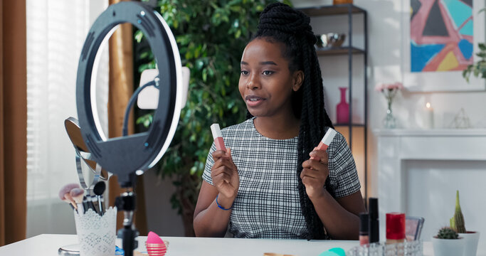 A female beauty blogger records a daily makeup tutorial using a ring light and a phone on a tripod, live streaming and comparing two shades of matte lipsticks. - Powered by Adobe