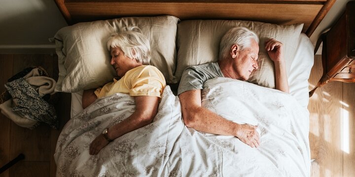 Elderly couple sleeping in bed at home. Peaceful rest for elderly man and woman. Senior couple enjoying sleep. Cozy bedroom for elderly pair. Restful sleep for seniors in a bed in their home.