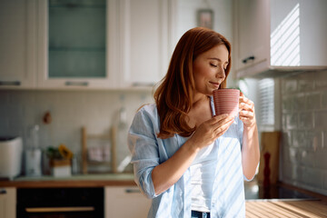 Smiling woman enjoying in smell of fresh coffee in kitchen.