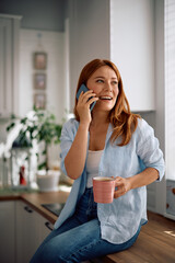 Happy woman talking on cell phone while drinking coffee at home