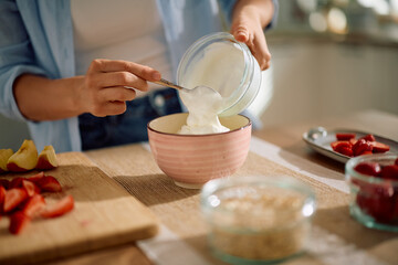 Close up of woman using Greek yogurt while making oatmeal at home.