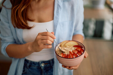 Close up of woman eating oatmeal topped with strawberries and apples in morning.