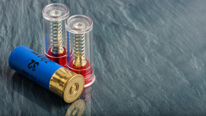 12 gauge shotgun shell in blue plastic case and two blank firing cartridges on gray granite background, space for advertising text
