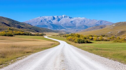 Fototapeta premium Winding road through autumnal countryside leading to majestic mountains