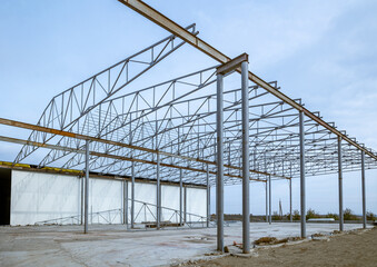 Fototapeta premium Installation of a steel frame under the sip panels of a warehouse with refrigeration chambers. Beams and roof rafters are mounted on the bearing supports. Foundation and concrete floor. Skeleton roof
