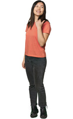 Full-body young Chinese woman points with thumb finger away, laughing and carefree.