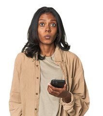 Young Indian woman using a smartphone shrugs shoulders and open eyes confused.