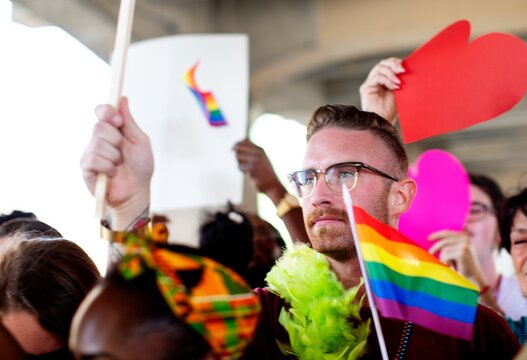 A diverse group of LGBTQ people at a pride parade. LGBTQ man with rainbow flag. LGBTQ man in pride parade, pride month celebration, LGBTQ man in pride parade, happy diverse people in pride parade - Powered by Adobe