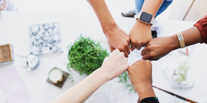 Diverse group of hands, including male and female, showing unity with a fist bump. Hands of different ethnicities female, huddle in unity. Unity and diversity. Environment and business concept.