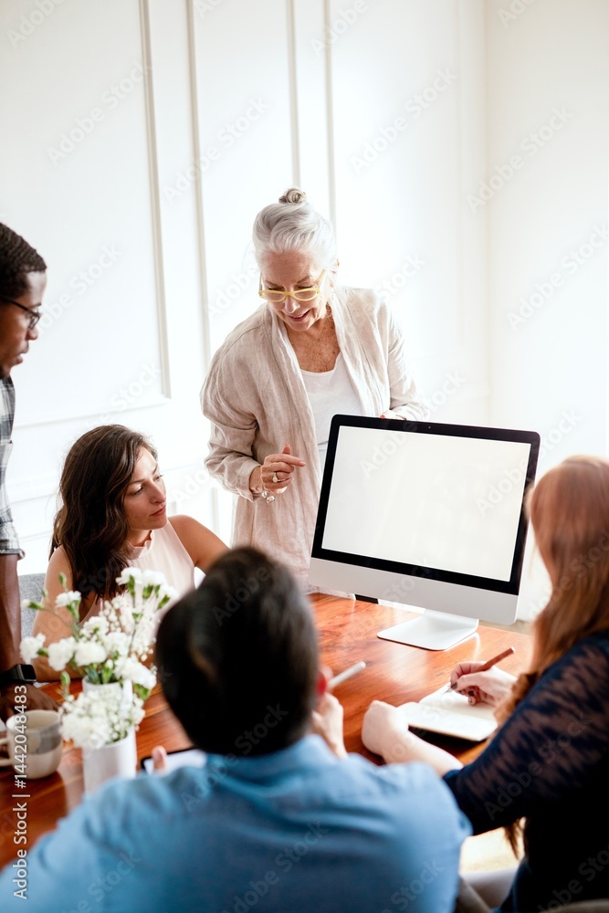 Poster group meeting with diverse team around a table. senior woman presenting on a computer. collaborative