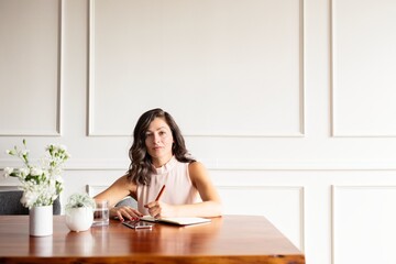 Young hispanic woman writing at a table. Woman with long hair writing notes. Woman at table with a notebook. Woman writing in a journal. Professional marketing execustive taking notes in an agenda.