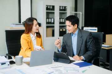 Two asian business workers talking on the smartphone and using laptop at office.