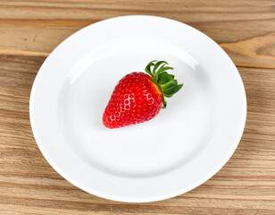 vibrant red strawberry sits clean white plate, showcasing its fresh and juicy appearance. natural shine and texture of fruit highlight its ripeness, evoking sense of freshness and deliciousness