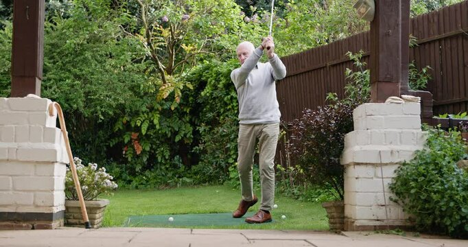 Mini golf, swing and senior man in backyard for sports, training and relax with hobby on artificial grass. Game, putting course challenge and club on lawn with stroke, hit and ball in garden of home.