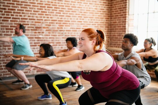 A diverse group of men and women doing squats in a fitness class. The fitness class includes people of different ethnicities, focusing on squats and exercise. Diverse group of people in fitness class