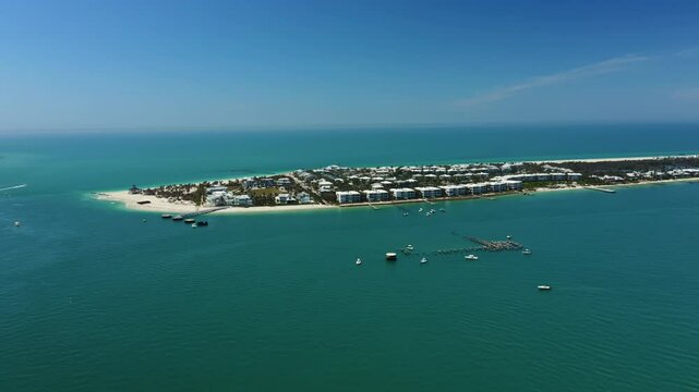 Boats anchor near docks along the southern beach of Gasparilla Island. White sand coastline curves behind a line of beachfront homes and calm turquoise Gulf waters.