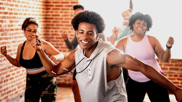 Group dance class with diverse participants enjoying energetic moves. Smiling individuals in casual workout attire, dancing in a bright studio with brick walls. Diverse people in wellness class at gym