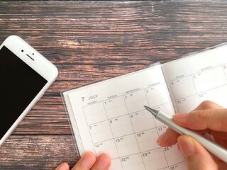 机上で7月のスケジュール帳に記入する手元とスマホ