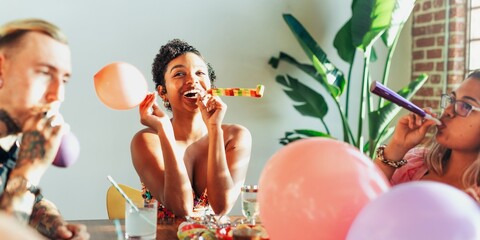 Group of diverse friends celebrating with balloons and party blowers. Joyful atmosphere with...