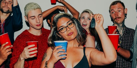Obraz premium Group of diverse young adults at a party, holding red cups, smiling, and having fun. Casual party scene with friends enjoying drinks and laughter. Diverse people drinking out of colorful cups at party