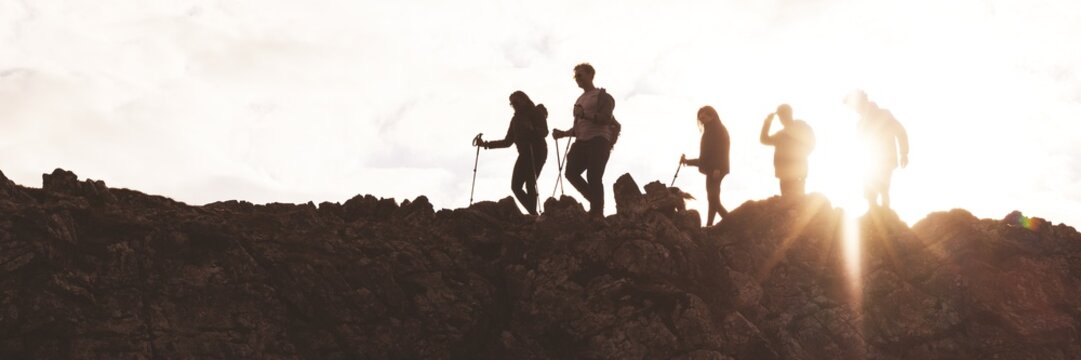 Silhouettes of hikers on a rocky ridge at sunset. Group of hikers with walking sticks. Adventure and exploration in nature. Hiking and trekking enthusiasts. Hiking adventure on mountain trail.