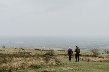 Two people hiking on a grassy hill under a cloudy sky. Hikers enjoy nature, walking on a trail. Scenic landscape with hikers exploring the outdoors. Senior couple on a hike in the countryside.